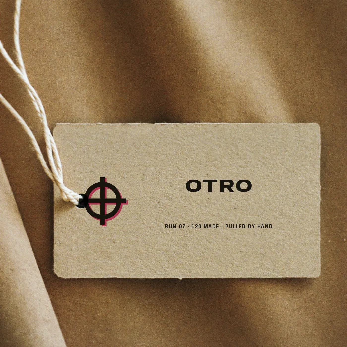 A sand cardboard swing tag printed with the OTRO target, the wordmark and the run number